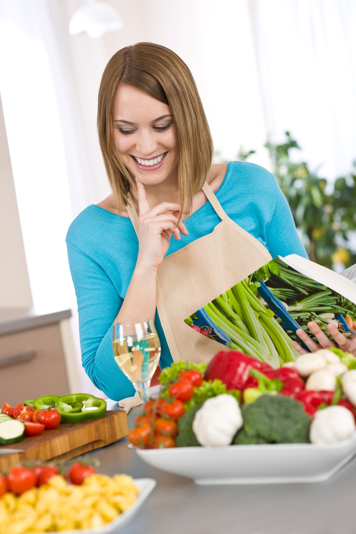 Eine Frau die in ein Kochbuch lachend schaut, vor Ihr Gemüse liegend auf den Tisch